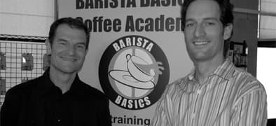 David and Matthew Gee, founders of Barista Basics Coffee Academy, in front of the Barista Basics banner